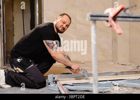 Construction worker cutting ceramic tile using tile cutter while working on bathroom renovation Stock Photo
