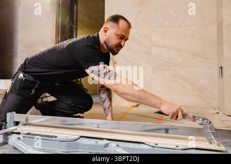 Construction worker cutting ceramic tile using tile cutter while working on bathroom renovation Stock Photo