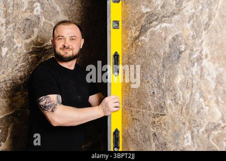 Builder checking the evenness of marble tiles with a level tool, ensuring precision and accuracy during renovation work on a wall Stock Photo