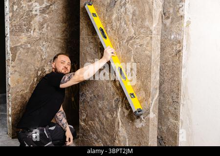 Builder checking the evenness of marble tiles with a level tool, ensuring precision and accuracy during renovation work on a wall Stock Photo