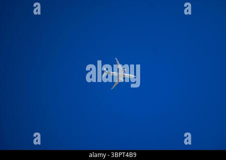 A commercial passenger jet soars through a deep blue sky, viewed from directly below. Stock Photo