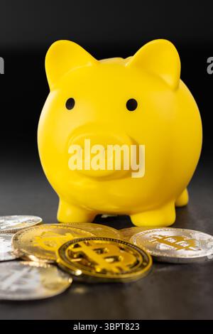 A yellow piggy bank surrounded by silver and gold Bitcoin coins on a textured gray surface. The image symbolizes digital currency, financial savings, Stock Photo