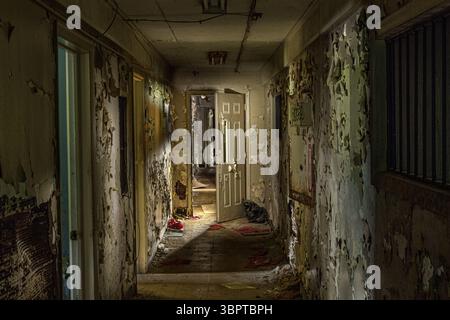 Rotting dirty hallway with peeling paint and door at the end in abandoned building, Indiana USA Stock Photo