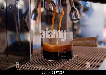 Close-up of freshly brewed espresso pouring into a measuring glass from a professional coffee machine. Stock Photo