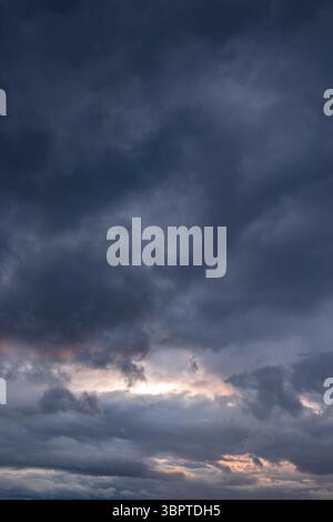 Heavy rain storm clouds building background backdrop with late evening sunlight shining through the clouds. Stock Photo