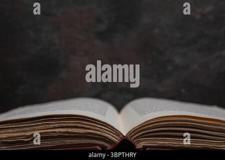 Symmetrical close-up of an open antique book with focus on printed text at bottom edge on dark textured surface. Stock Photo