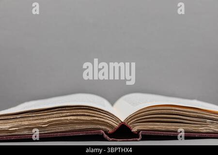 Open antique book positioned at bottom edge of frame with focus on deckled page edges, set against a light grey background in near-symmetrical view Stock Photo