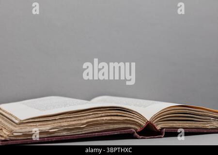 Open antique book with uneven deckled page edges on dark textured surface and light grey background; text blurred by shallow focus. Stock Photo