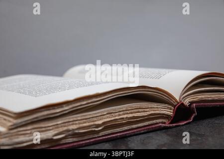 Close angled view of open antique book with deckled page edges in focus, placed on dark surface with light grey background and shallow depth of field Stock Photo