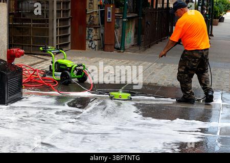 A worker power washing a New York City sidewalk with a Greenworks Pro 3000psi electric pressure washer Stock Photo