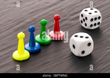 Colored game tokens and two white dice with black dots on a dark background Stock Photo