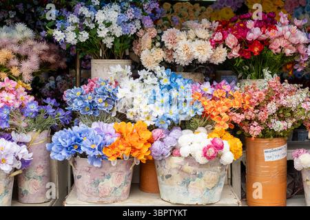 Colorful artificial flowers in decorative pots arranged closely together at a market stall, showcasing vibrant hues and textures. Stock Photo