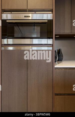 Close-up of a modern stainless steel microwave oven built into dark wood kitchen cabinets. Elegant and functional appliance in a luxury home interior. Stock Photo