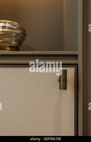 Close-up of a modern textured brass handle on a beige leather-paneled cabinet door. Luxurious furniture detail in a contemporary interior design. Stock Photo
