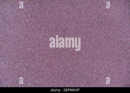 Macro view of a rough purple textured surface. Granular and speckled background, similar to sandpaper or asphalt. Abstract and minimalist wallpaper. Stock Photo