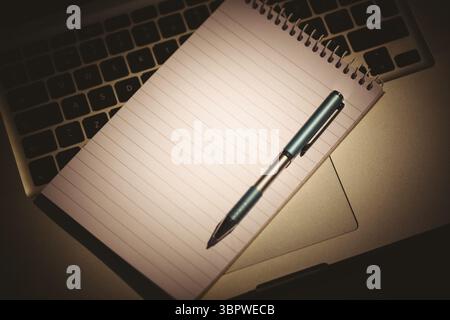 Vector art showing notepad lying across laptop keyboard palm rest with ballpoint pen casting shadow Stock Photo