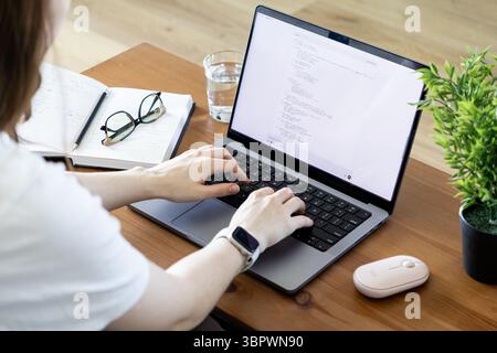 Poznan, Poland - June 15, 2025: Over-the-shoulder view of a young person's hands typing programming code on a laptop keyboard, depicting a modern digi Stock Photo