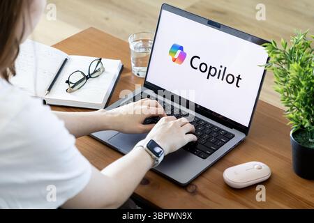 Poznan, Poland - June 15, 2025: Copilot AI assistant software displayed on a modern laptop, with user hands actively typing on keyboard, emphasizing d Stock Photo