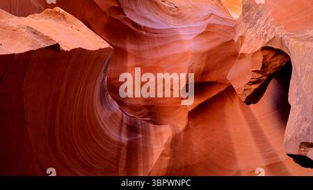 Sunlight filters through narrow sandstone curves in Antelope Canyon, revealing vibrant orange and red waves etched by centuries desert wind and water. Stock Photo