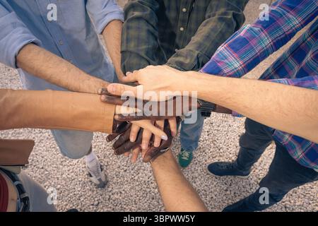 A diverse multiethnic group of friends or colleagues stacking their hands in the center in a circle, symbolizing teamwork, unity, support, trust and a Stock Photo