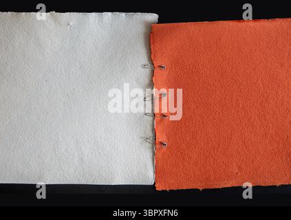 Red and white textured paper stitched together with safety pins on black background. Stock Photo