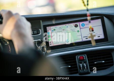 Padua, italy 8 july 2025, modern car dashboard with navigation system and music player displaying on screen while driver is holding steering wheel Stock Photo