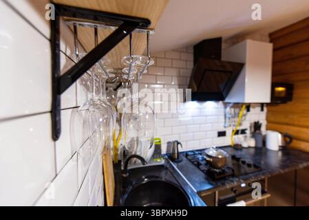 Modern kitchen with wine glasses hanging on a rack, white subway tiles, and black countertop. Stock Photo