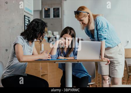 Three female colleagues reviewing meeting notes and feedback in bright office cafeteria Stock Photo