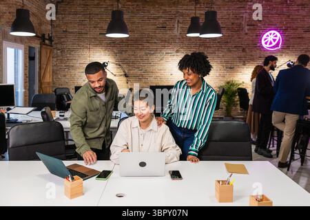 Multi ethnic team collaborating on laptop in modern office Stock Photo