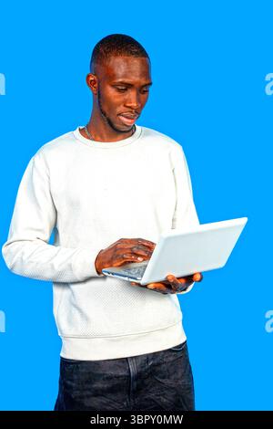 Young man concentrating on his laptop, working remotely against a vibrant blue backdrop Stock Photo