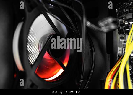 Computer's internal components featuring tangled wires and a glowing cooling fan illuminated by red-orange RGB lighting. Stock Photo