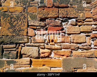 old stone wall with mustard yellow, orange and ochre-colored old bricks of different sizes Stock Photo