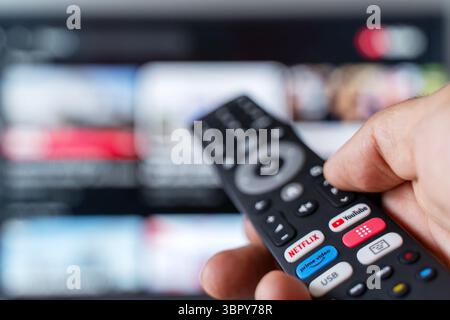 Tbilisi, Georgia - July 2, 2025: Close-up photo of a smart TV remote control featuring dedicated buttons for popular streaming platforms like Netflix, YouTube, and Amazon Prime, with a television screen blurred in the background. Represents modern digital media consumption, subscription-based services, and on-demand entertainment. Ideal for tech, streaming, binge-watching, or media lifestyle content. Stock Photo