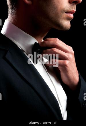 A man in a suit is adjusting his bow tie. Stock Photo