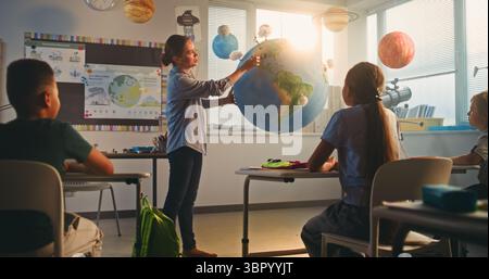 STEM Class on Renewable Energy: Female Teacher Explaining Energy Resources to Elementary School Students Using Model of Planet Earth. Diverse Kids Learning Geography and Science in Modern Classroom. Stock Photo