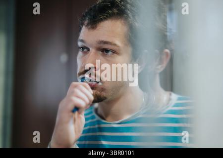 Young man brushing teeth in front of a mirror, focusing on oral hygiene Stock Photo
