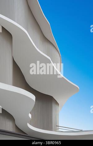 Dynamic, low-angle view of a futuristic building with flowing, wave-like white balconies. Abstract, parametric architecture with organic forms against Stock Photo