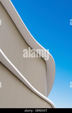 Graceful curves of a modern, minimalist building facade against a vibrant blue sky. Abstract architectural background with flowing lines and ample cop Stock Photo