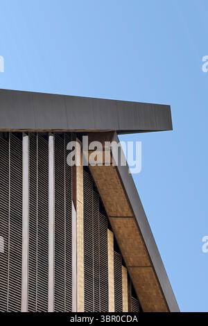 Abstract architectural detail of a modern building's roofline and louvered facade against a clear blue sky. Features strong geometric lines, angles, a Stock Photo