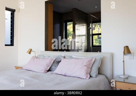 Queen bed resting with gray duvet, pillows in master bedroom opening into glass shower with towel. Luxury, serenity, minimalist, interior, comfort, el Stock Photo