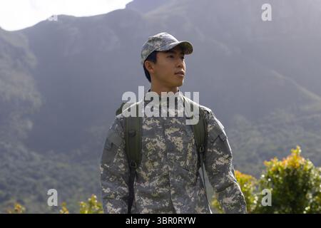 Asian male soldier standing in mountain area wearing camouflage uniform and carrying green backpack. Military, adventure, tactical, rugged, outdoor, r Stock Photo