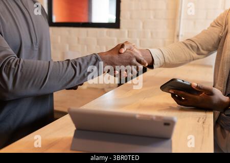 African American business associates shaking hands over tablet, payment terminal at retail checkout. Professional, collaboration, modern, commercial, Stock Photo