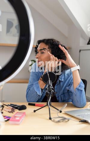 African American non-binary individual applying eyebrow pencil at loft desk with ring light mic. Studio, creativity, modern, beauty, technological, pe Stock Photo