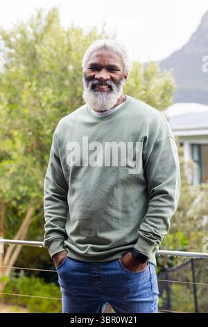 African American senior man leaning on railing at terrace wearing sweatshirt, smartwatch and jeans. Philosophical, contemplative, leisure, outdoor, ru Stock Photo