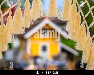 A close-up view of decorative tassels framing a blurred yellow house in the background. Stock Photo