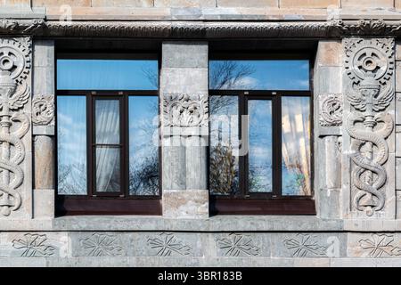 Two rectangular windows with brown frames against a wall of gray blocks with an ornament. From the Windows of the World series. Stock Photo
