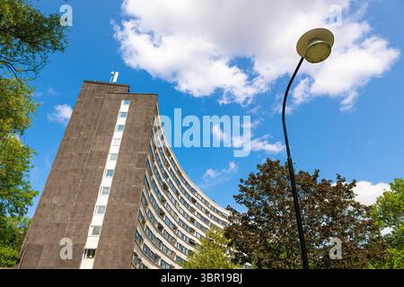 Stockholm, Sweden - June 5, 2025: A modern curved building with a textured concrete facade, trees and a bright blue sky with fluffy white clouds. A st Stock Photo