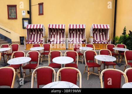 Vaxholm, Sweden - June 4, 2025: A row of striped beach chairs with cushions, arranged in front of red bistro tables and chairs. Stock Photo