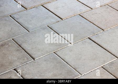 A close-up view of a textured concrete floor with rectangular tiles arranged in a staggered pattern. The surface appears smooth with subtle variations Stock Photo