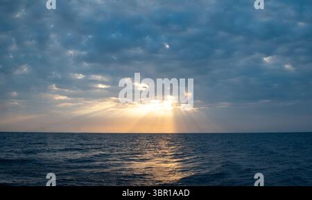 Soft rays of sunlight peek through a cloudy sky over the ocean. Stock Photo